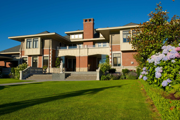 Large estate home in brick and shingle siding, viewed across manicured lawn with a central tiered fountain and formal landscaping with blue hydrangeas